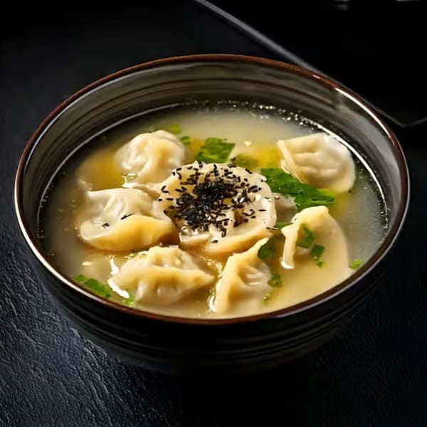 A bowl of Korean mandu-guk (dumpling soup) with green onions and black sesame seeds.