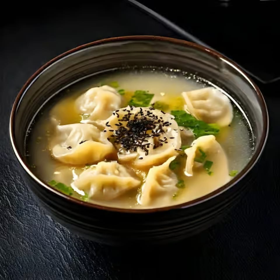 A bowl of Korean mandu-guk (dumpling soup) with green onions and black sesame seeds.