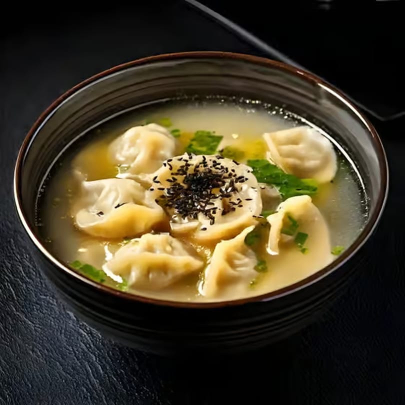 A bowl of Korean mandu-guk (dumpling soup) with green onions and black sesame seeds.