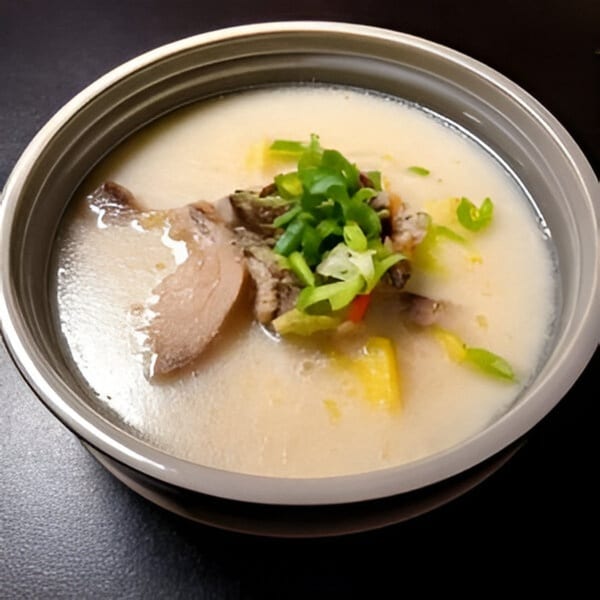 A bowl of Korean Seolleongtang, a milky white ox bone soup, garnished with green onions and meat.
