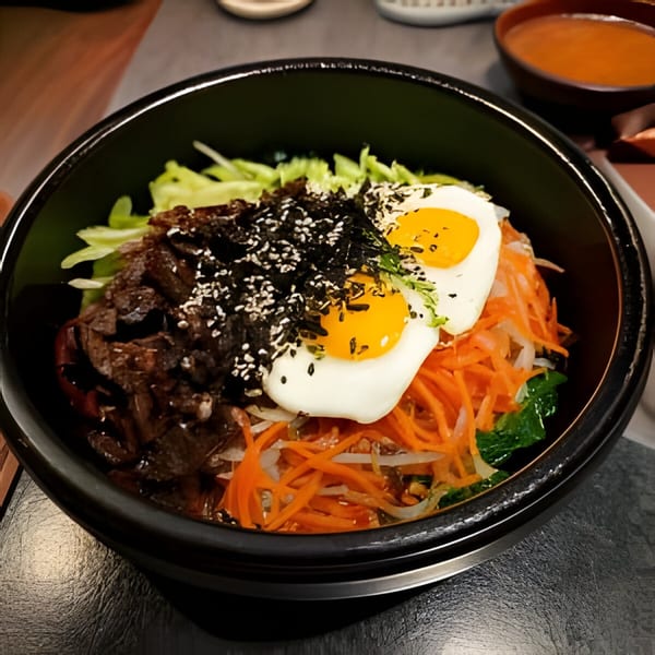 A black bowl of Jang Mo Gip bibimbap with beef, vegetables, and two fried eggs.