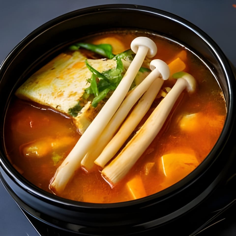 A black bowl of Korean stew with tofu, mushrooms, and green herbs in a rich orange broth.